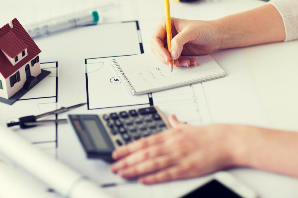 gros plan sur une main de professionnel de l'immobilier avec un plan et des outils architecturaux calculant une estimation